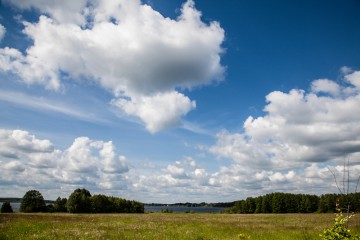 Man sieht eine grüne Wiese und in der Ferne einen See. Das ist der Blankensee. Am Himmel sieht man große Wolken. © Anke Großklaß/team red